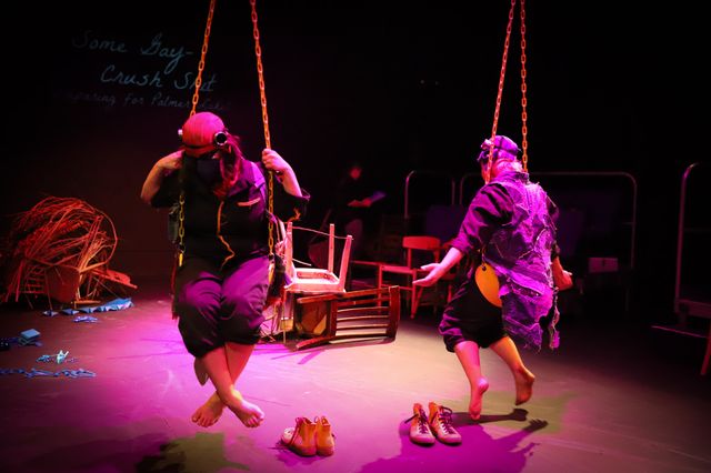 Bower bird dancers twisting and untwisting on yellow swings in purple theater lighting