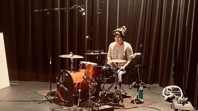 Sondra sitting behind the drum kit, surrounded by mics and cables, ready to record